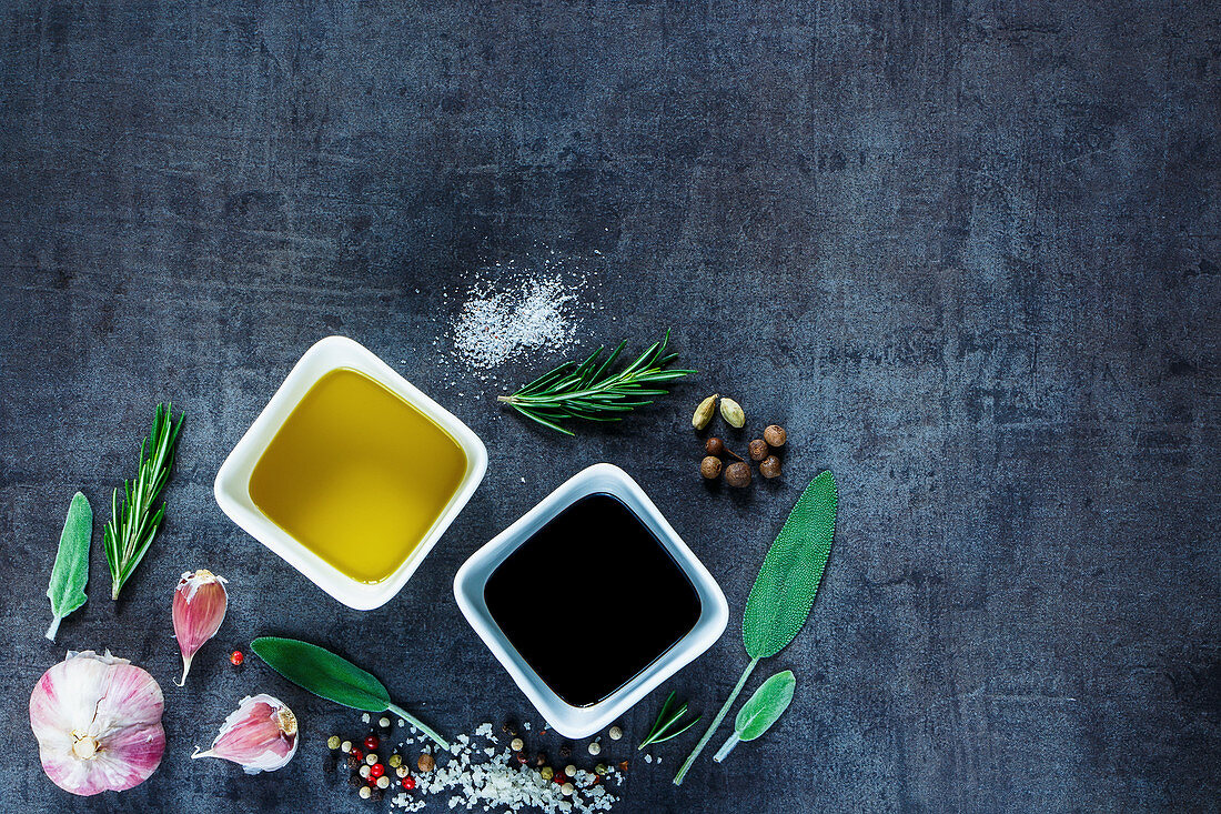 Top view of Olive oil and vinegar with peppercorns, sea salt, garlic and rosemary on dark vintage background
