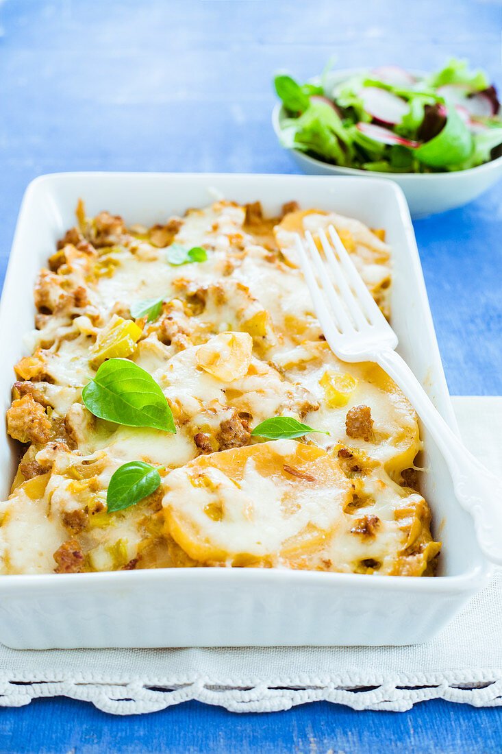 Kartoffelauflauf mit Würstchen und Lauch in Auflaufform, mit Salat serviert