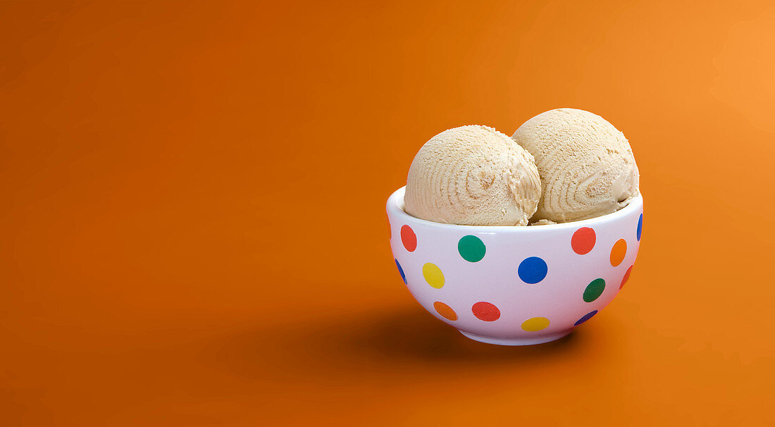 Two scoops of caramel ice cream in a spotted bowl