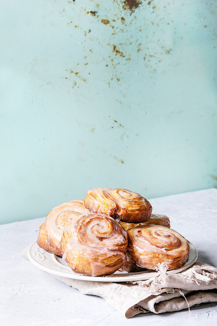 Plate of homemade glazed puff pastry cinnamon rolls on cloth over grey table
