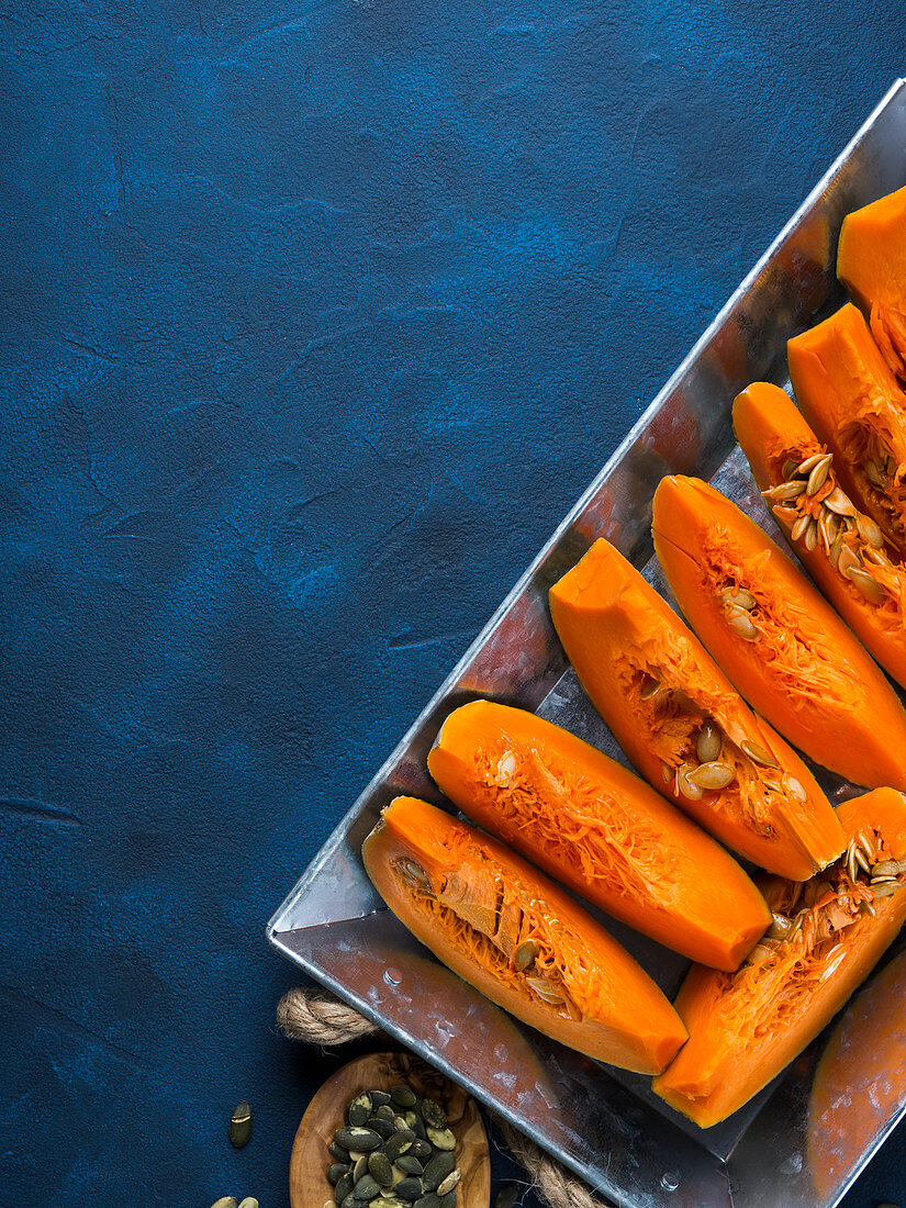 Raw sliced pumpkin ready to be cooked on a tray over blue background