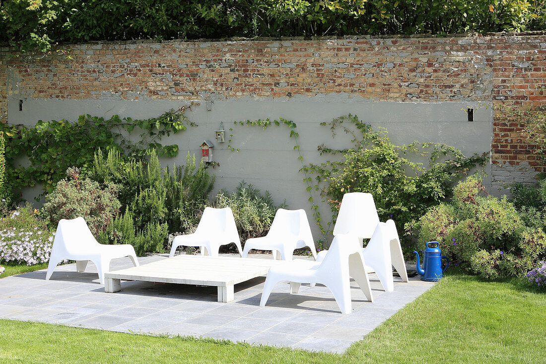 White plastic chairs on terrace in front of garden wall