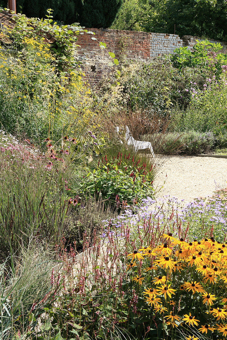 Naturnaher Staudengarten mit Weg und Mauer im Spätsommer