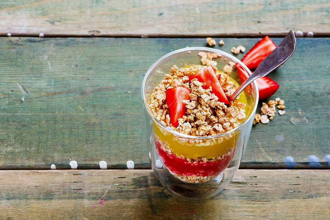 Healthy vegan granola breakfast: Muesli, mango and strawberry layered parfait on wooden table background