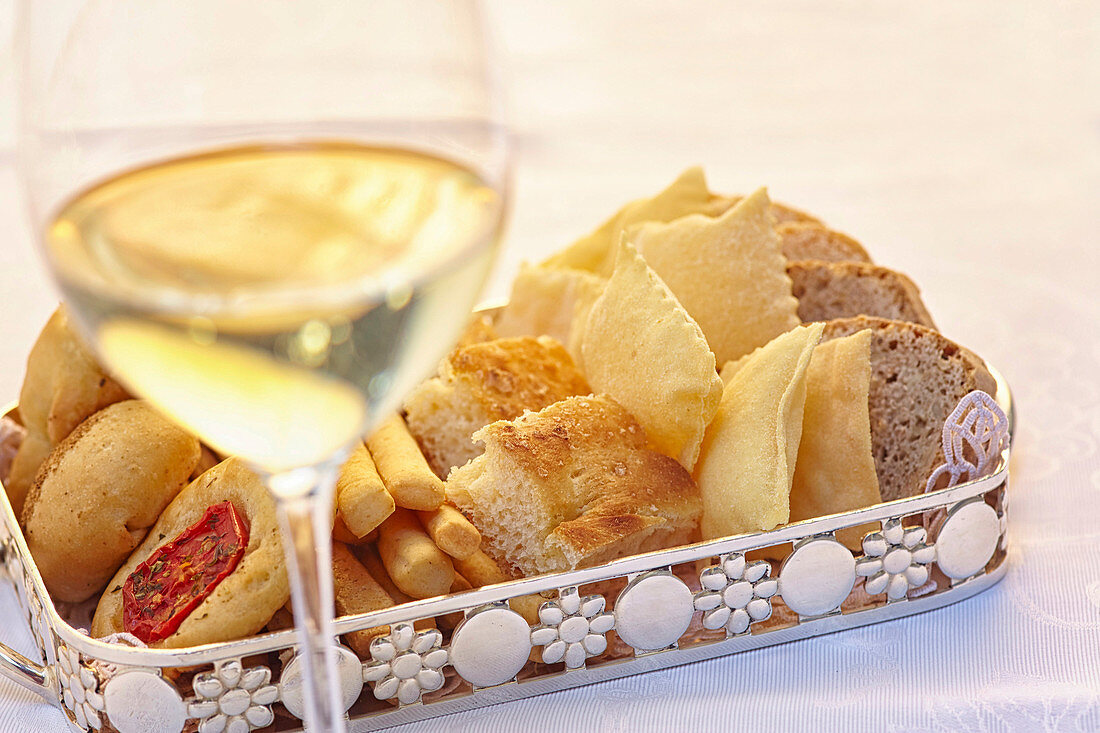 Brot und Gebäck in einem Tablett davor ein Glas Weißwein