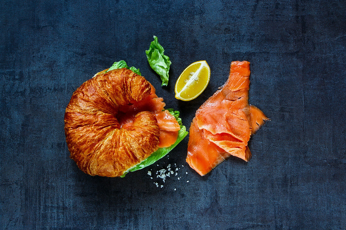 Croissant mit Räucherlachs auf dunkelblauem Untergrund (Aufsicht)