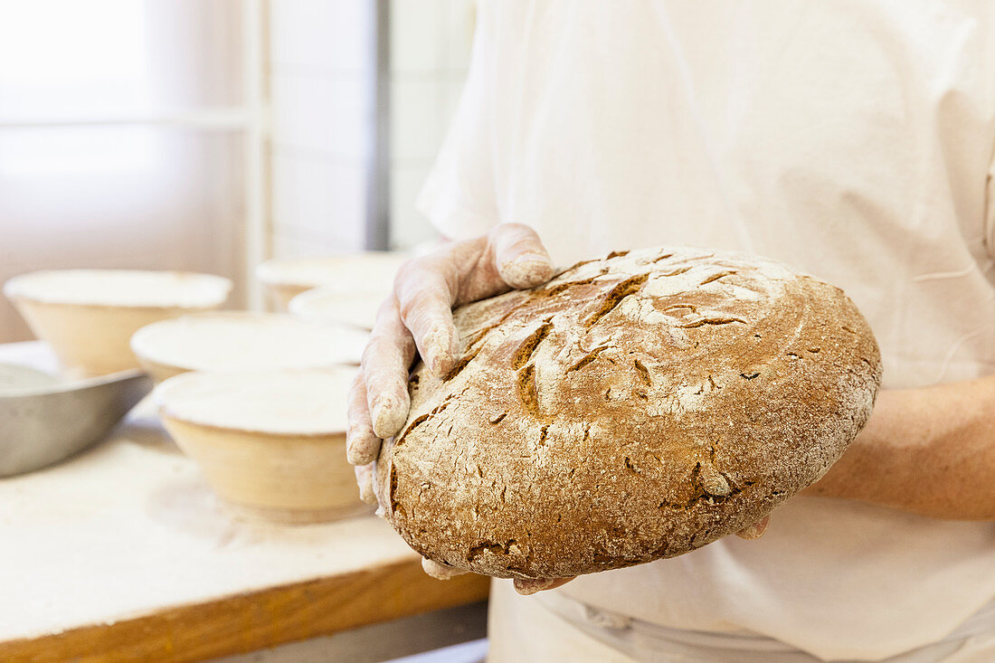 Bäcker hält frisch gebackenen Brotlaib in den Händen