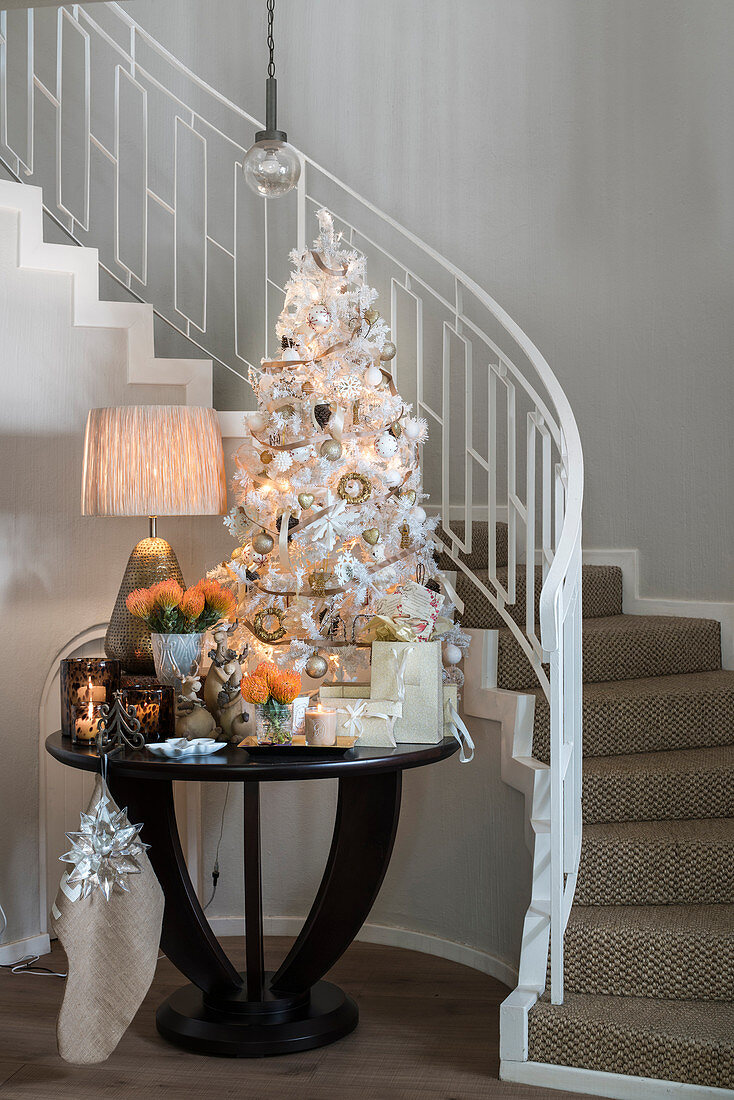 Tisch mit weißem Weihnachtsbaum und festlicher Deko vor der Treppe
