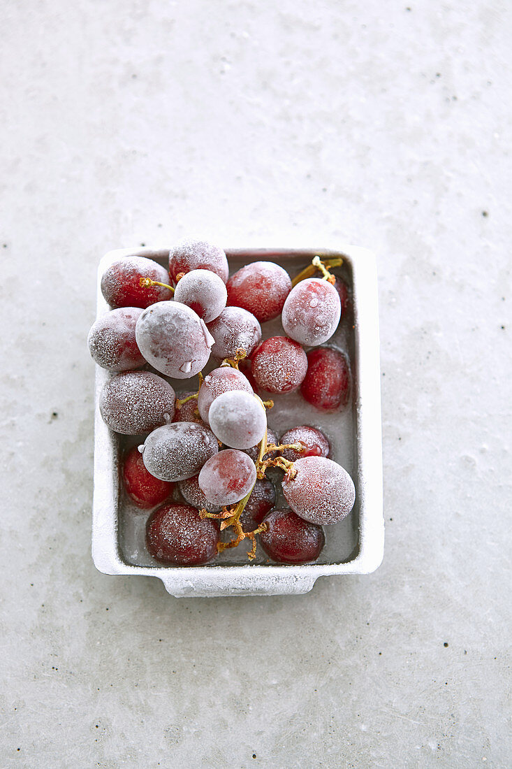 Frozen grapes in a metal dish on a concrete surface