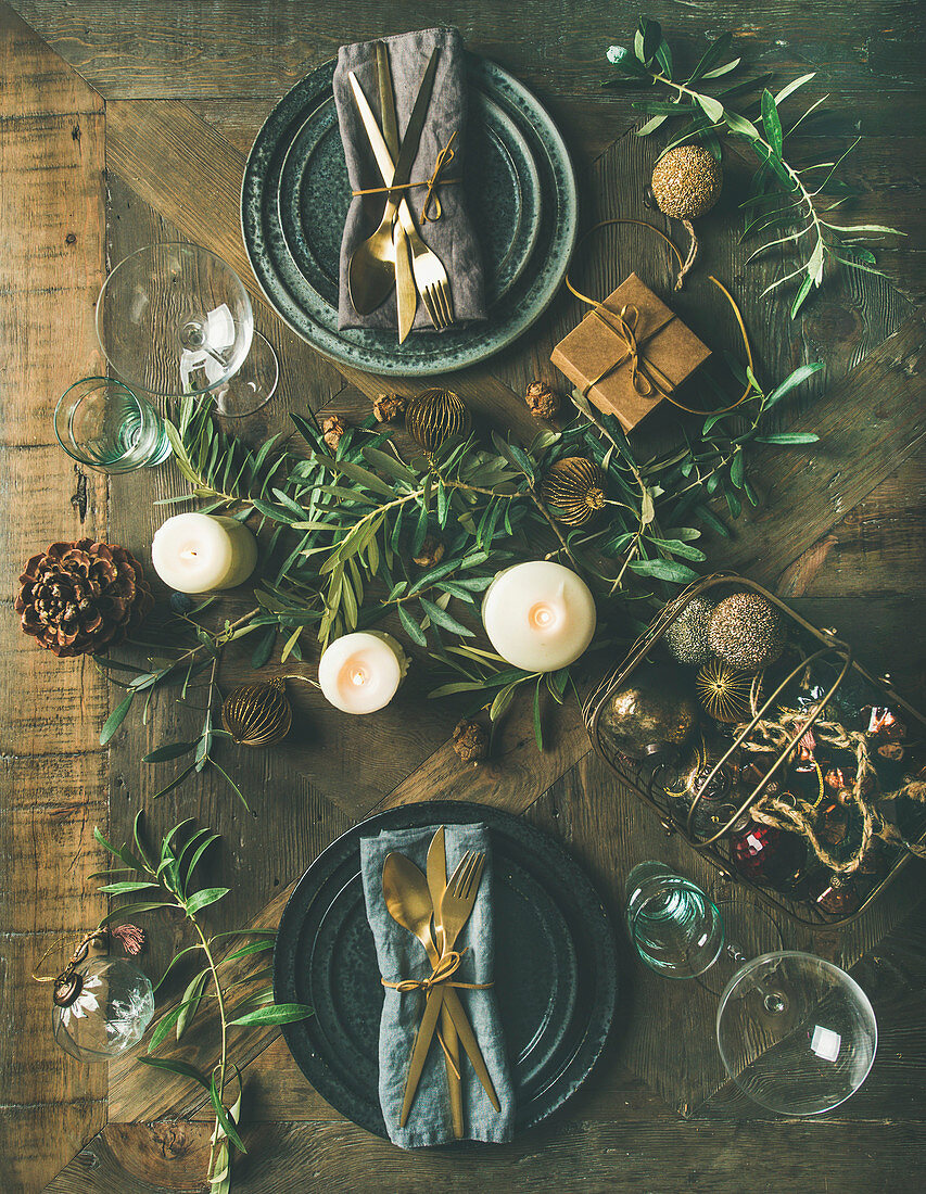 Christmas or New Years eve holiday table setting: Flat-lay of plates, silverware, glassware, candles, olive branches and toy festive decorations