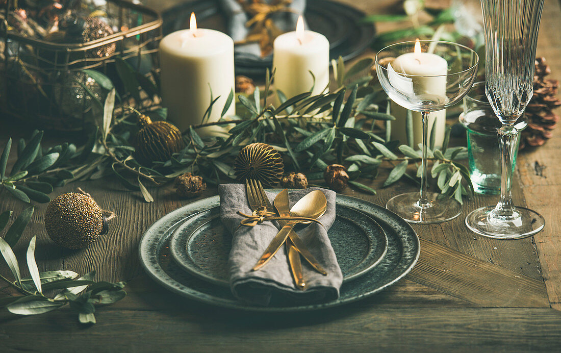 Christmas or New Years eve holiday table setting: Plates, silverware, glassware, candles, olive branches and toy festive decorations