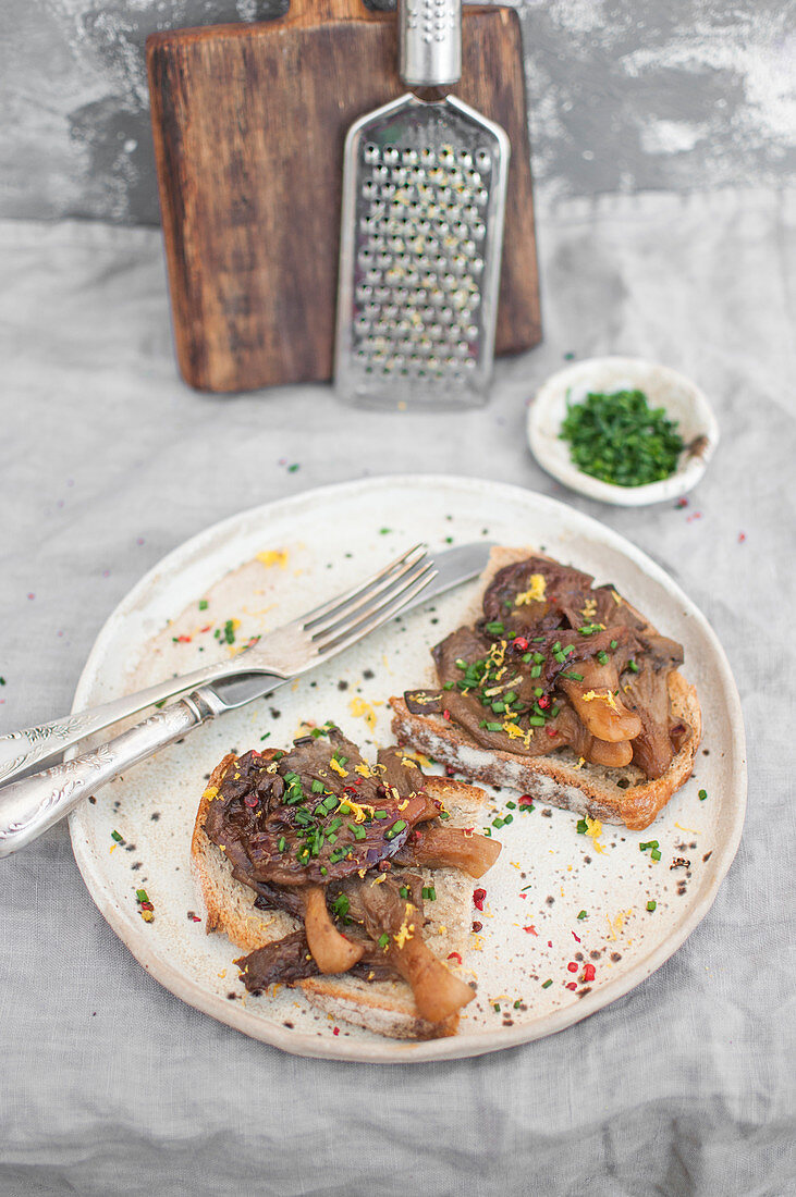 Teriyaki oyster mushrooms served on toasts, topped with lemon zest, pink pepper and chopped chives (Vegan)