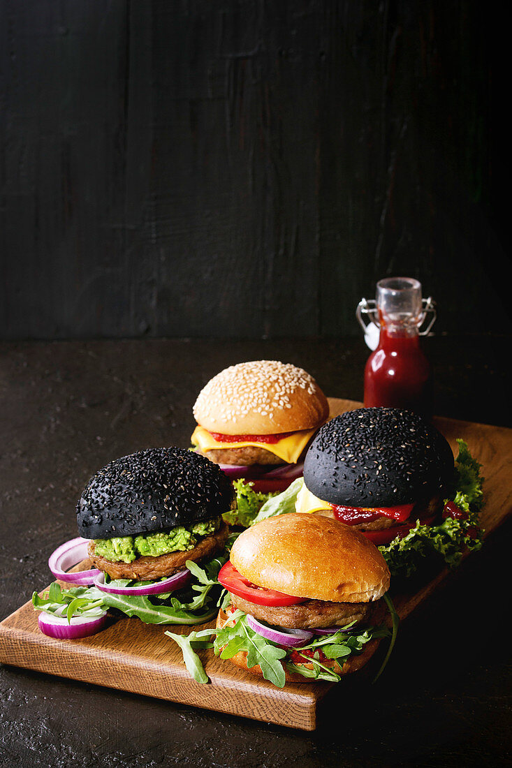 Verschiedene Burger mit hellen und schwarzen Burgerbrötchen auf Holzbrett