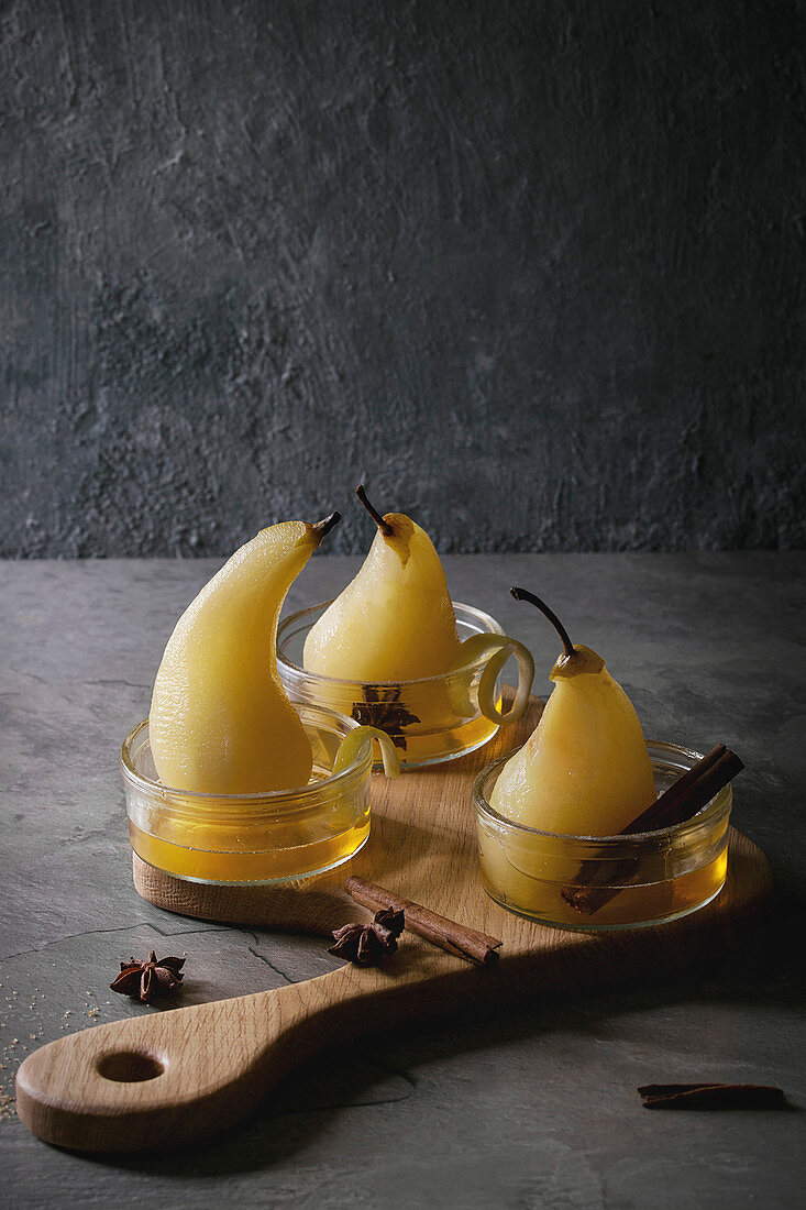 Traditional dessert poached pears in white wine served in glass bowls with syrup and lemon zest on wooden serving board