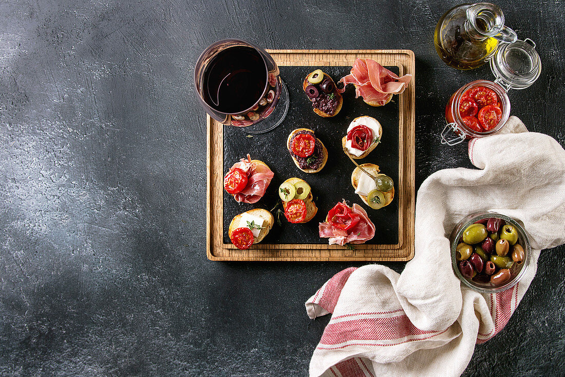 Tapas or bruschetta variety: Bread with ham prosciutto, sun dried tomatoes, olive oil, olives, pepper on slate wood serving board