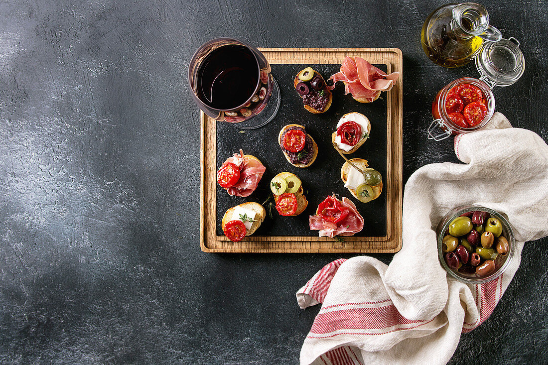 Verschiedene Bruschetta mit Schinken, Tomaten und Oliven serviert mit Rotwein