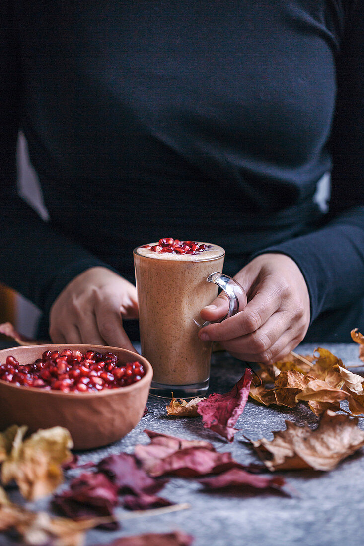 Frau trinkt Bananen-Mandelbutter-Smoothie mit Granatapfelkernen