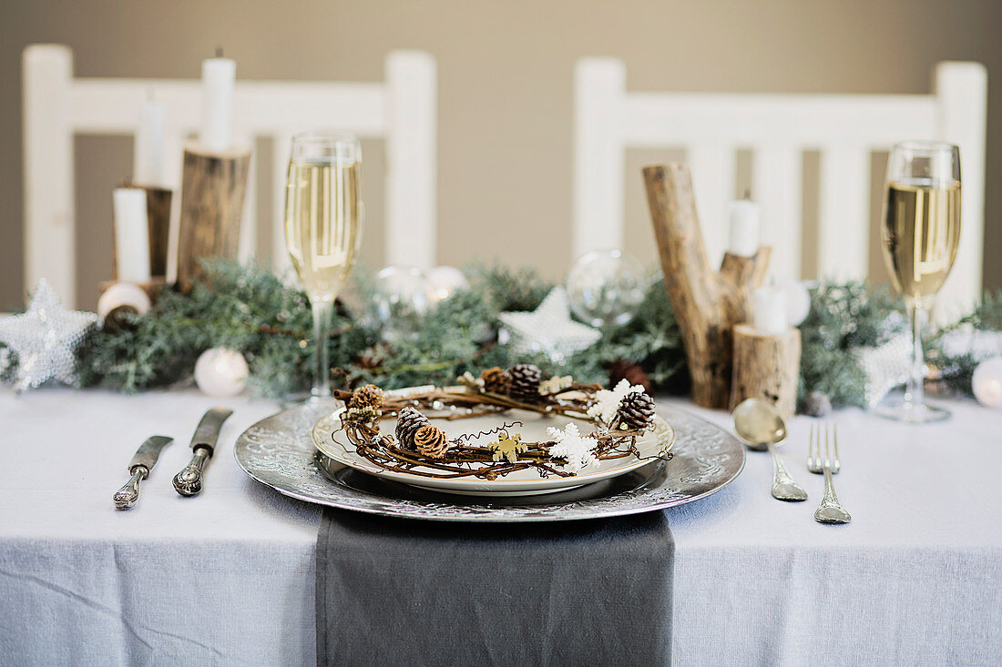 Festliches Weihnachtsgedeck mit Silbertellern und Zapfenkranz