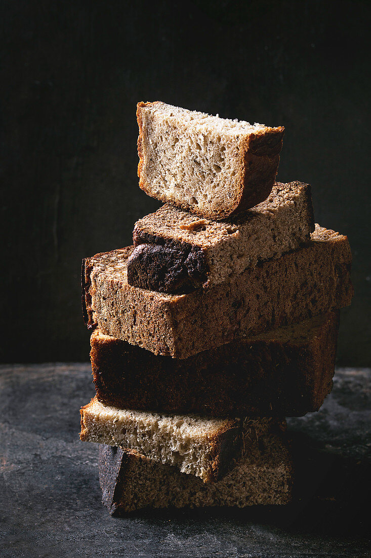 Variety loaves of sliced homemade rye bread whole grain and seeds in stack over old dark background