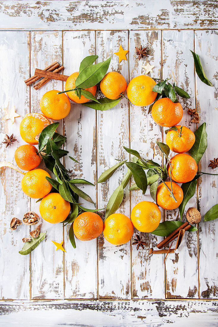 Clementines tangerines with leaves as Christmas wreath with cinnamon sticks and anise over white wooden plank background
