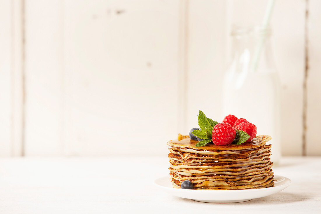 Milk and Stack of pancakes topped with berries and honey