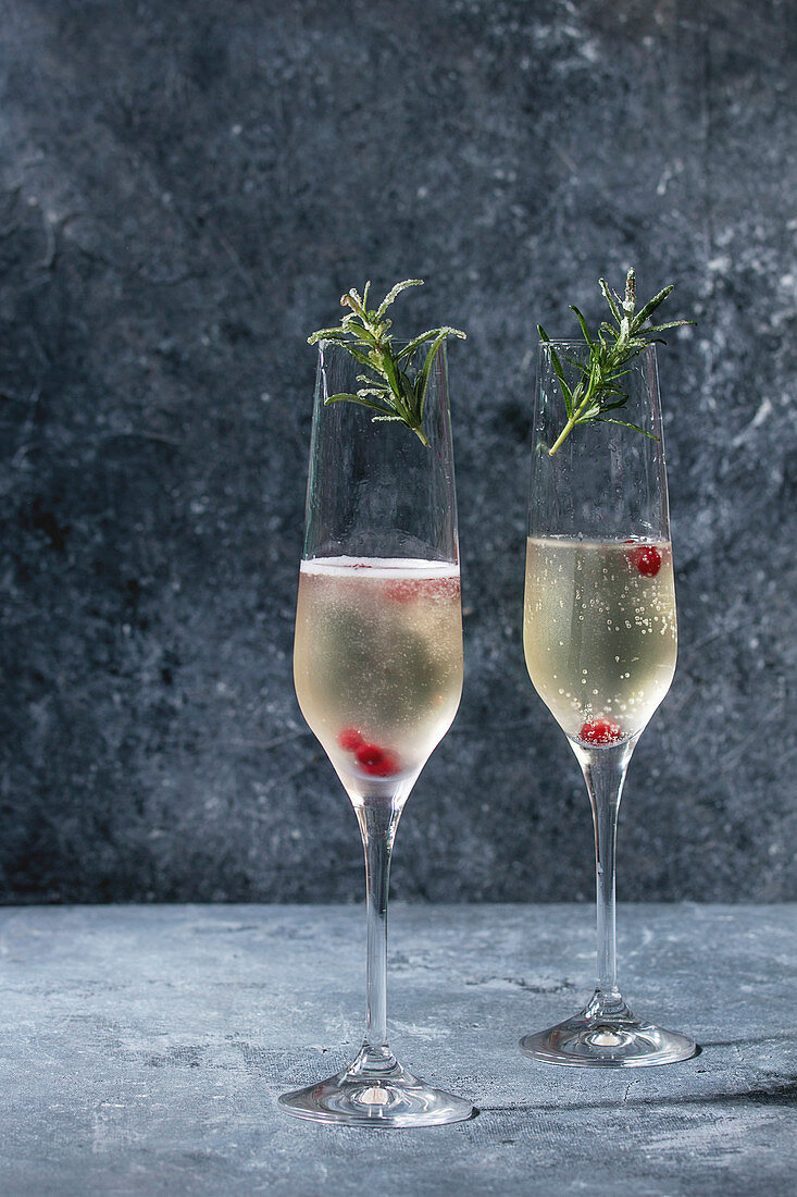 Zwei Gläser Champagner serviert mit roten Beeren und Rosmarin