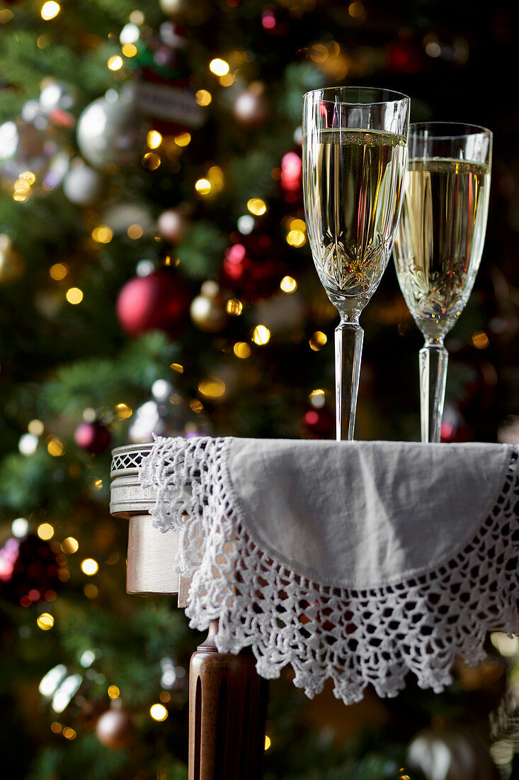 Champagne flutes on a table, with a Christmas tree behind