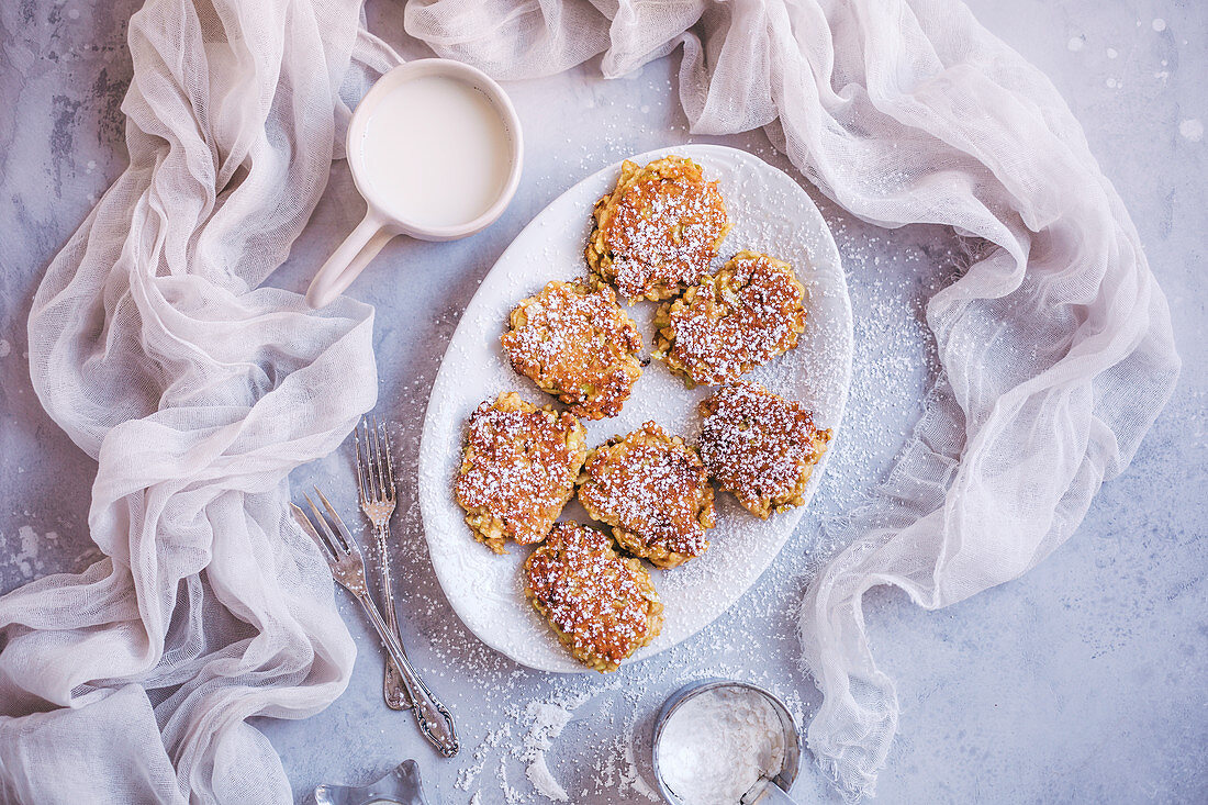 Sweet apple fritters sprinkled with powdered sugar on a white serving plate