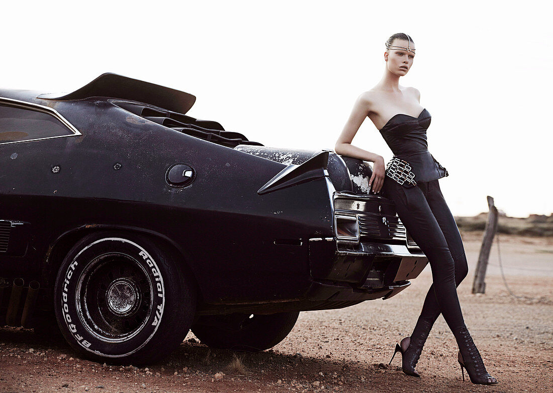 Brünette Frau in schwarzem Mieder und Lederleggins an schwarzem Auto stehend