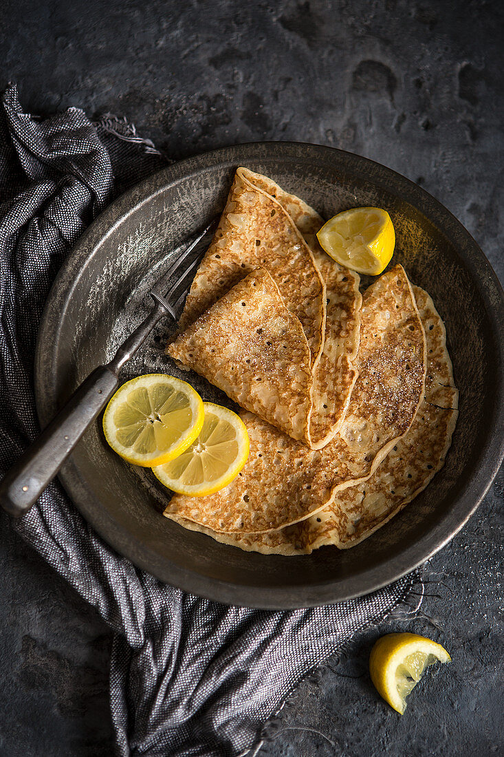 Two crepes with lemon slices on an antique plate