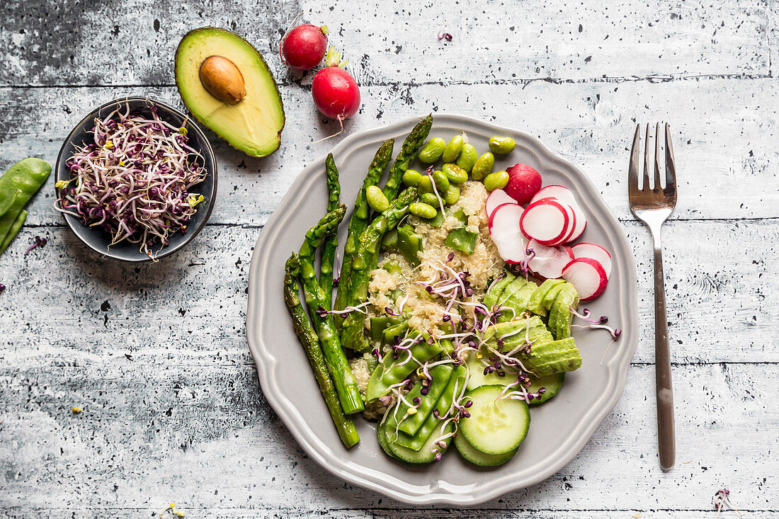 A green salad plate with bulgur wheat, asparagus, avocado, radishes, cucumber, mangetout, edamame and red sprouts