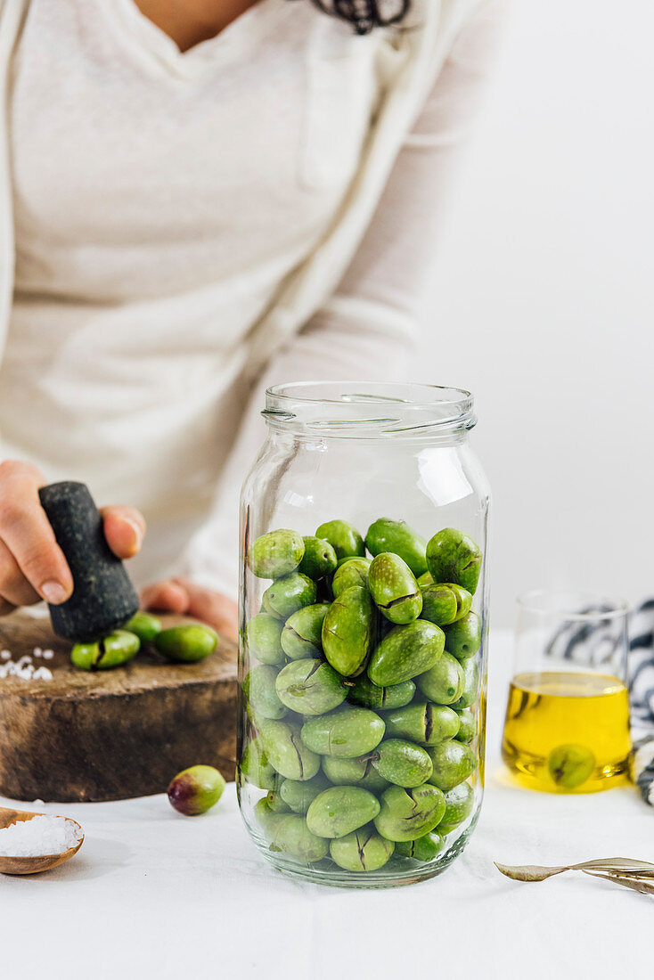 Oliven zum Einlegen vorbereiten: Frau zerstösst grüne Oliven mit Stössel