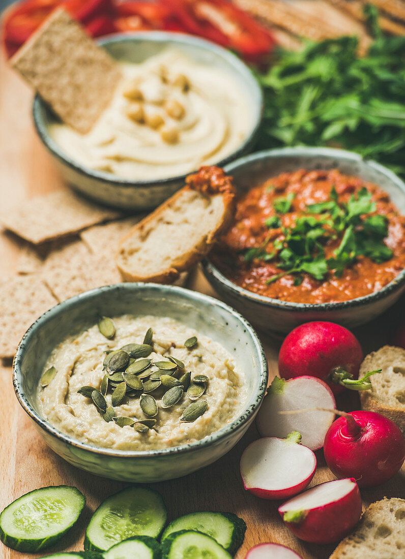 Various Vegetarian dips: hummus, babaganush and muhammara with crackers, bread and fresh vegetables, wooden background