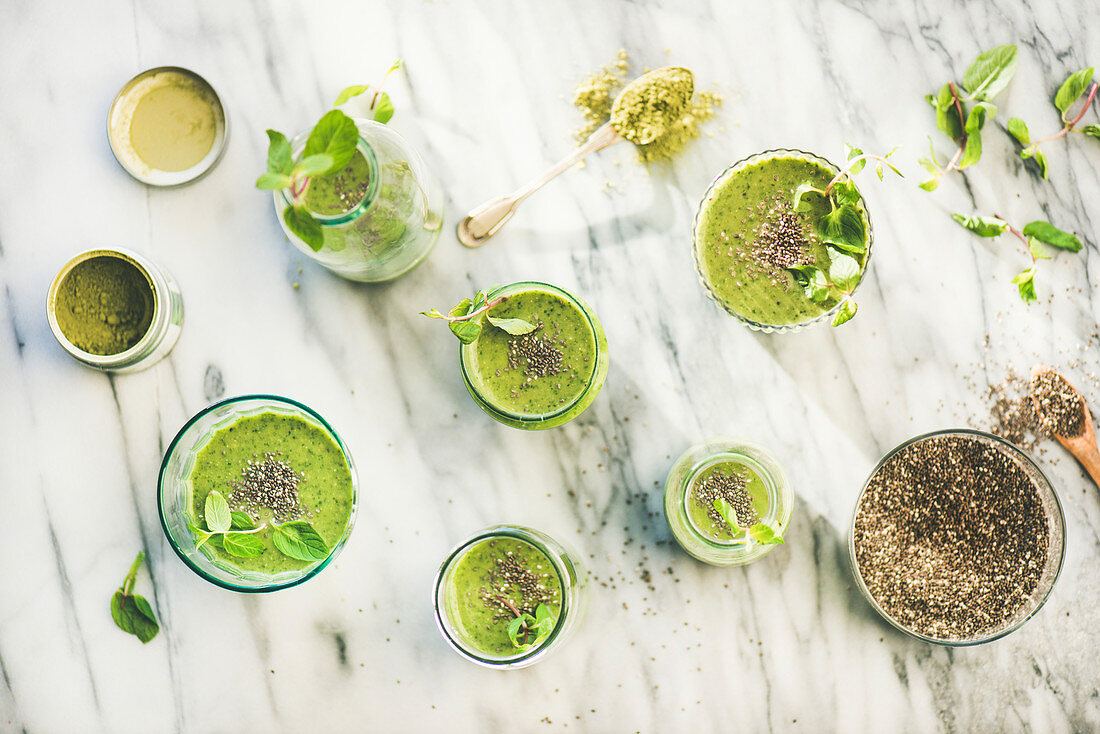Matcha green vegan smoothie with chia seeds and fresh mint in glasses and bottles over marble background