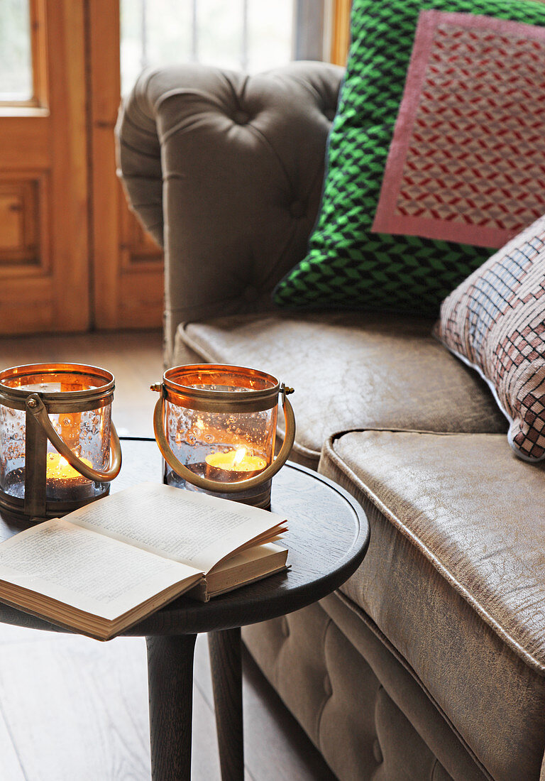 Open book and two candle lanterns on table next to sofa