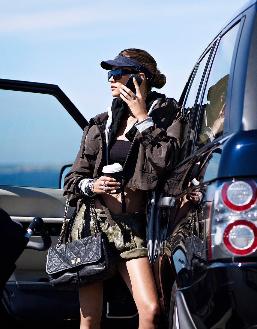 A young woman with a cup of coffee and a smartphone by a car
