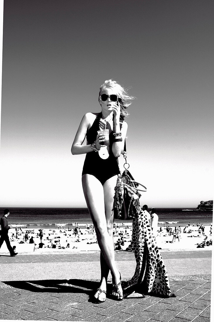 A blonde woman wearing a bathing suit with a drink on a beach (black-and-white shot)