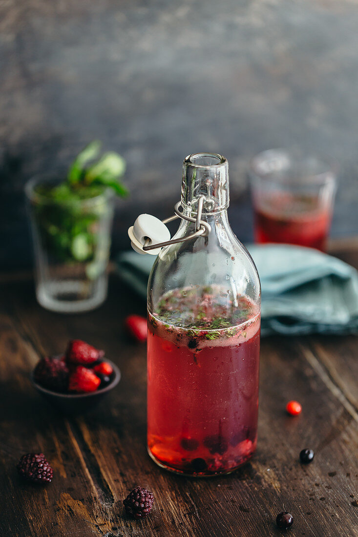 A refreshing drink with wild berries and mint in a glass bottle