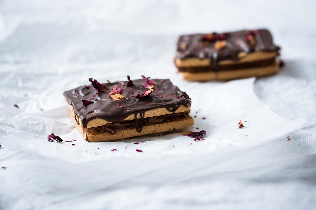 Biscuits with cocoa cream, chocolate icing and dried rose petals (vegan)