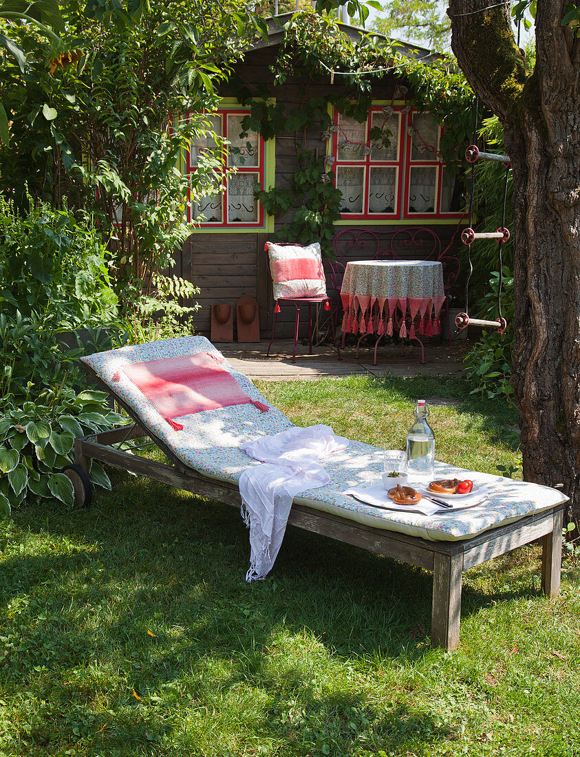 Liege mit Polster im Garten vor einem Holzhäuschen