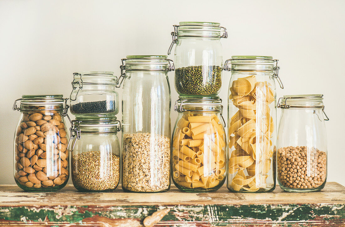 Getreide, Nudeln, Hülsenfrüchte und Mandeln in Vorratsgläsern auf Holztisch