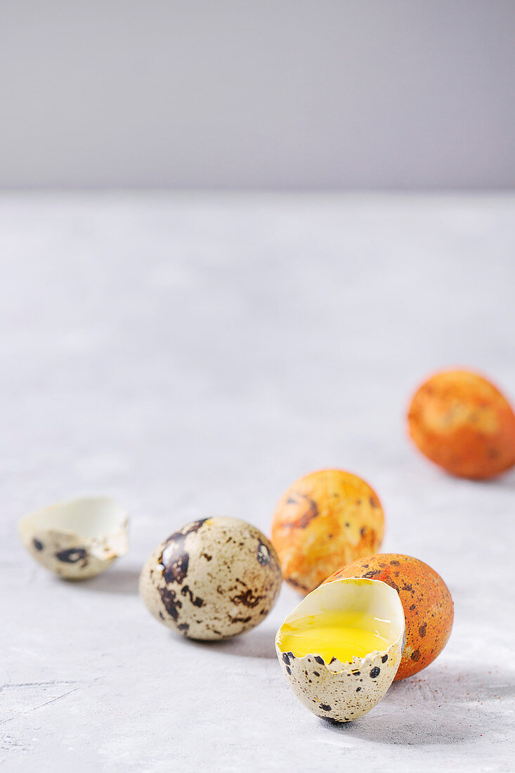 Easter greeting card with colored yellow orange quail eggs with yolk and shell over white texture background