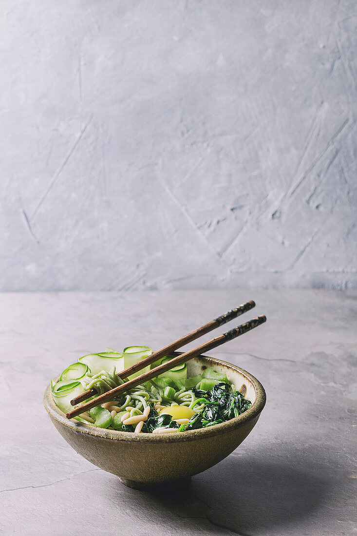 Ceramic bowl with vegetarian green pea noodles with sliced cucumber, celery, spinach, quail egg yolk, pine nuts served with wooden chopsticks