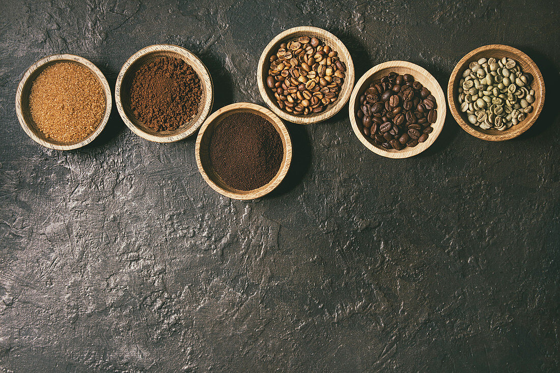 Brauner Zucker, Kaffeepulver und verschiedene Kaffeebohnen in Schälchen