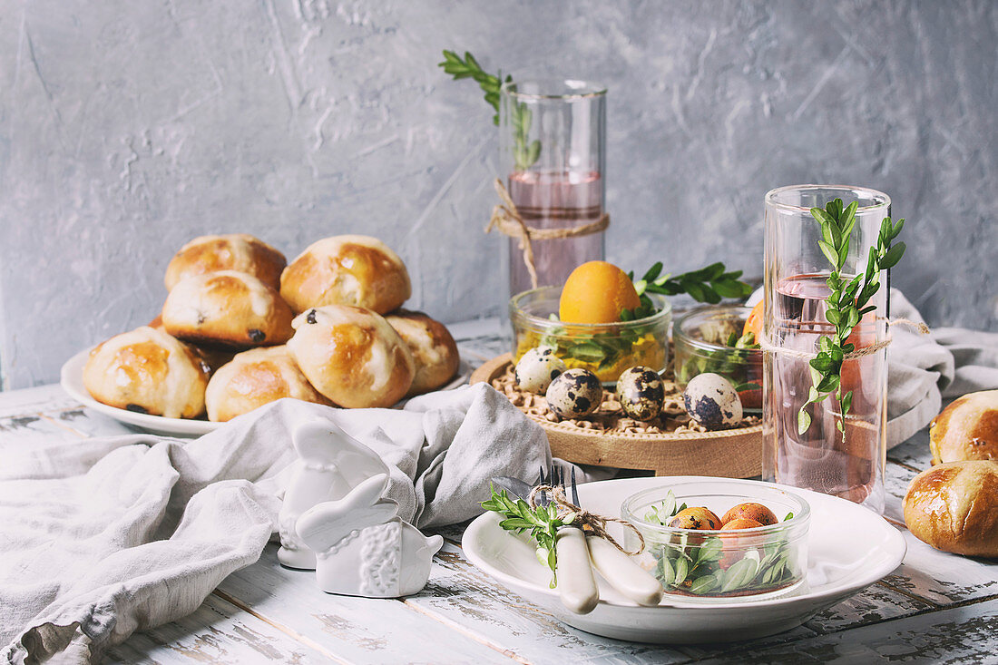 Hot Cross Buns auf gedecktem Ostertisch mit Eiern und Getränken