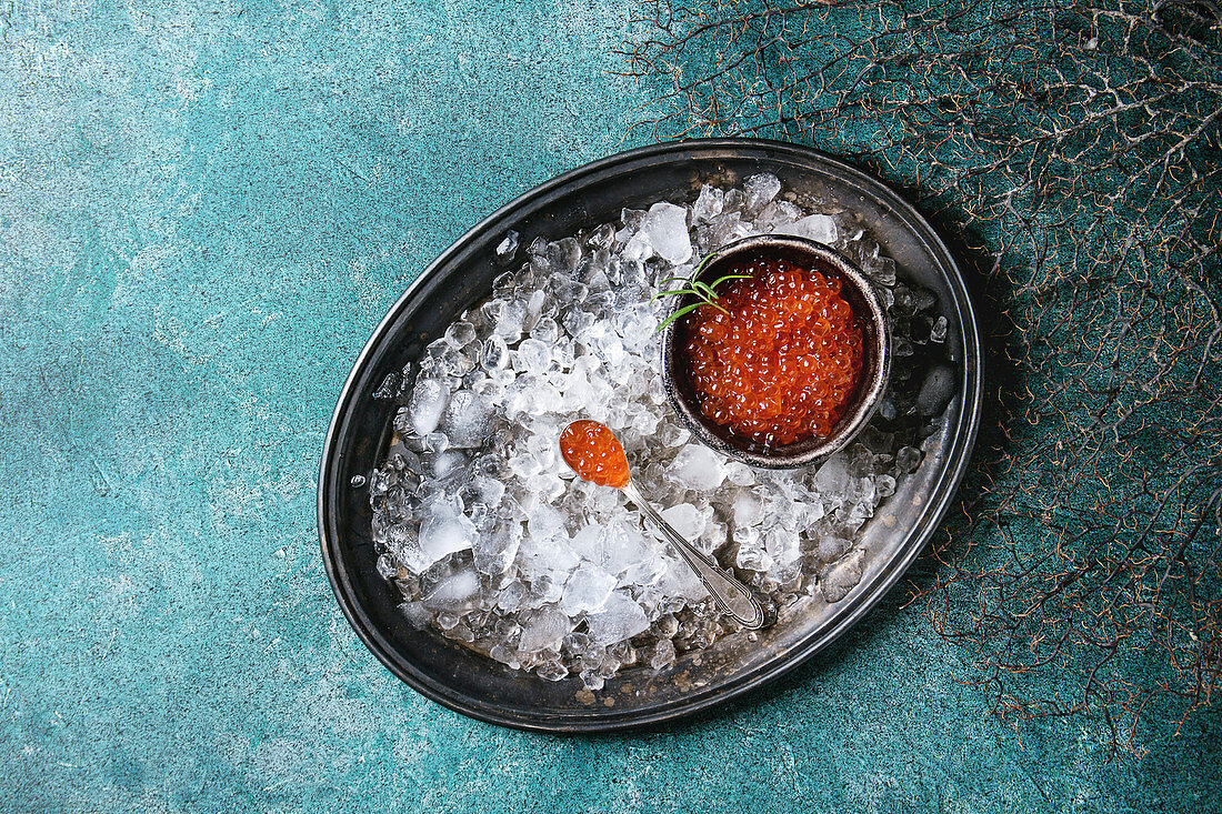 Bowl of red caviar on vintage metal tray with ice over turquoise texture background