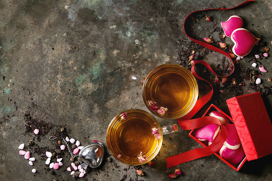 Valentinstag: Zwei Tassen Tee mit Rosenblüten daneben Herzplätzchen in Geschenkschachtel