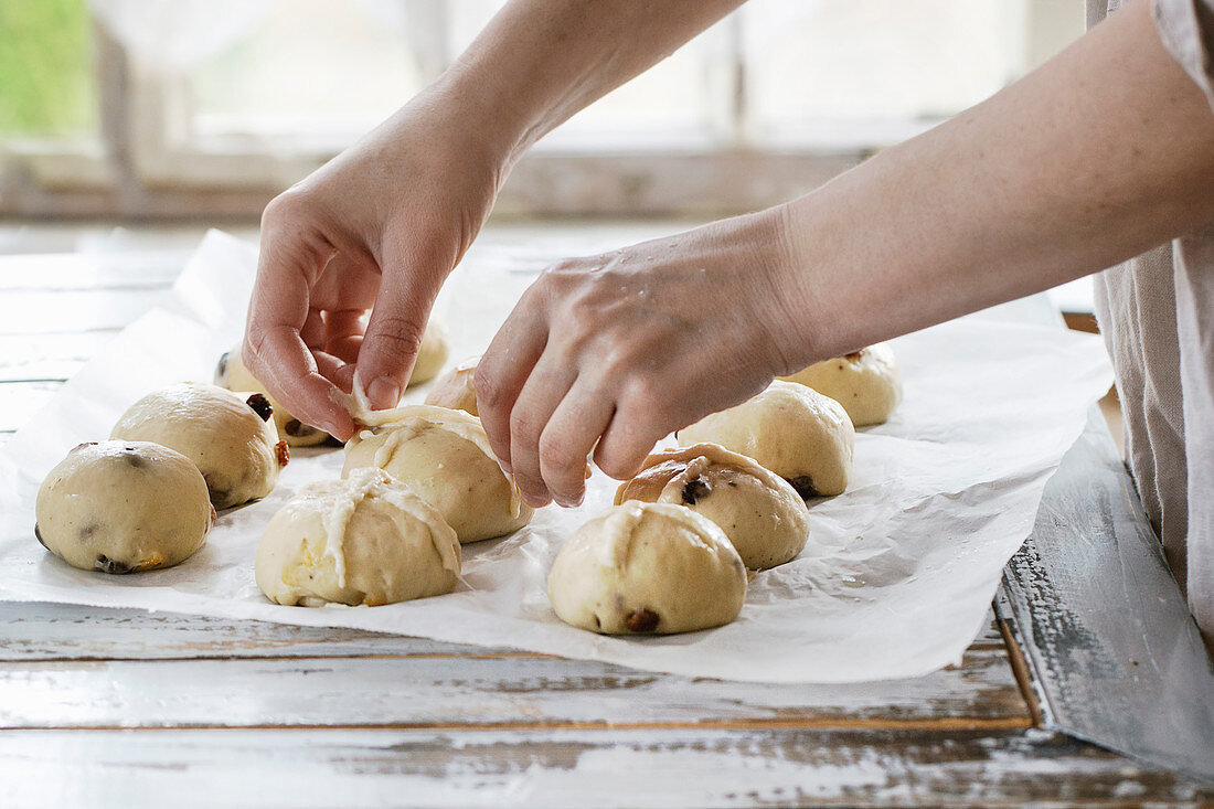 Raw unbaked buns. Ready to bake homemade Easter traditional hot cross buns on baking paper over white wooden table