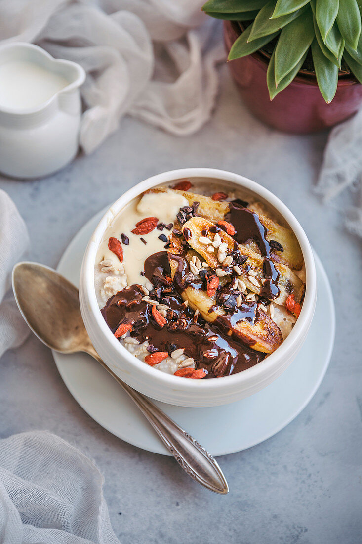 Bowl of porridge topped with caramelized bananas, melted chocolate, cacao nibs, goji berries and sunflower seeds