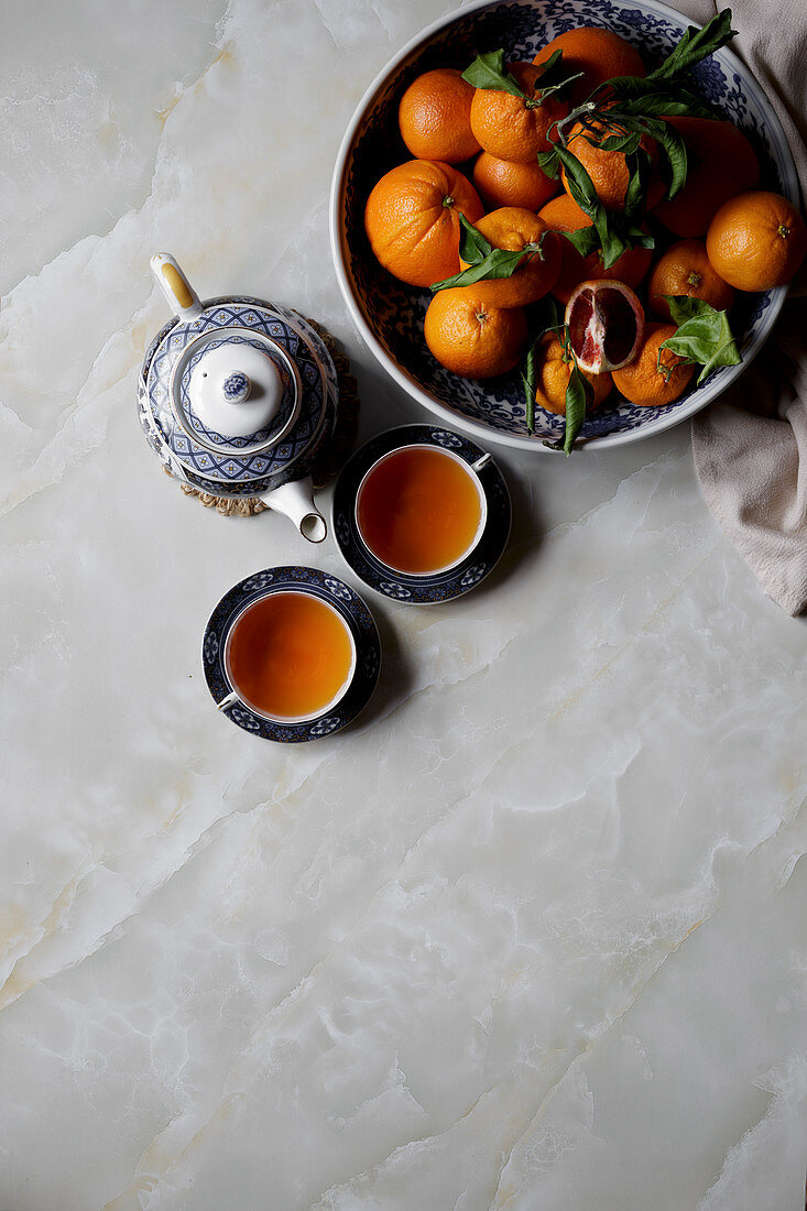 Tee in Teekanne und Teetassen, daneben Schale mit Orangen (Aufsicht)